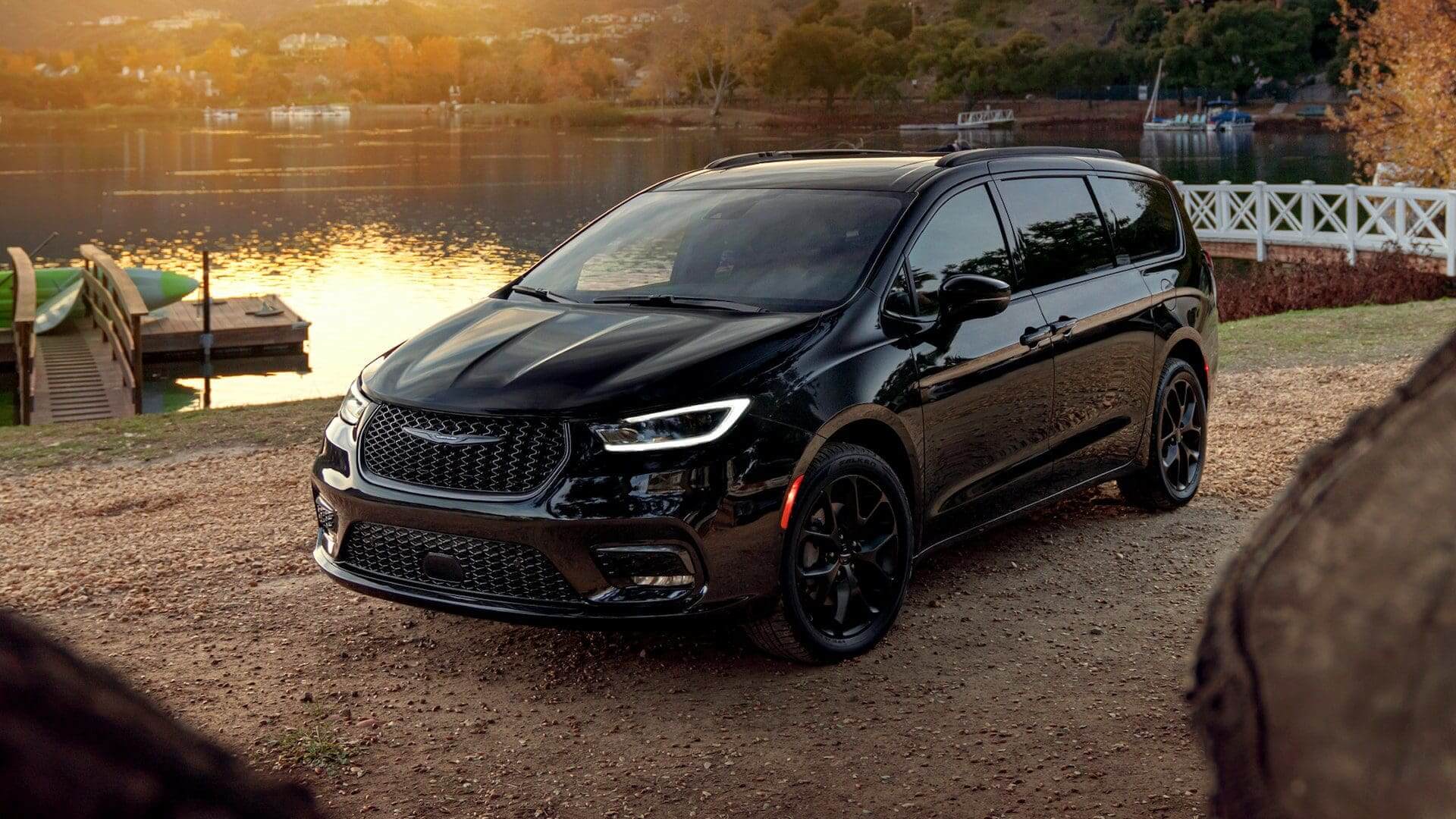 Sleek black luxury car parked by a serene lakeside during sunset.