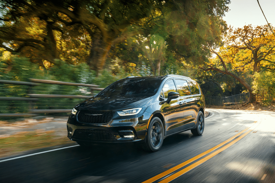 A black minivan driving on a tree-lined road during sunset.